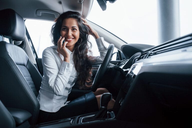 A smiling woman on a phone call in the driver's seat of a car
