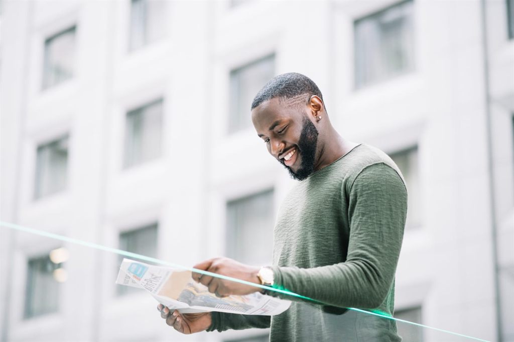 A smiling man reading a newspaper outside an office building