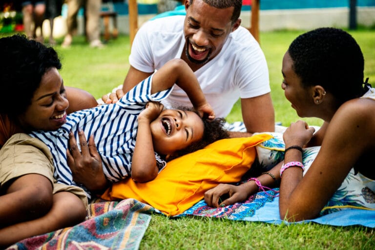 A family laughing together on a picnic blanket in a garden